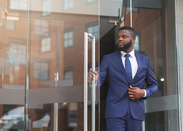 man in business suit exiting glass doors with confidence showcasing professional style and presence for success in business 2 ways